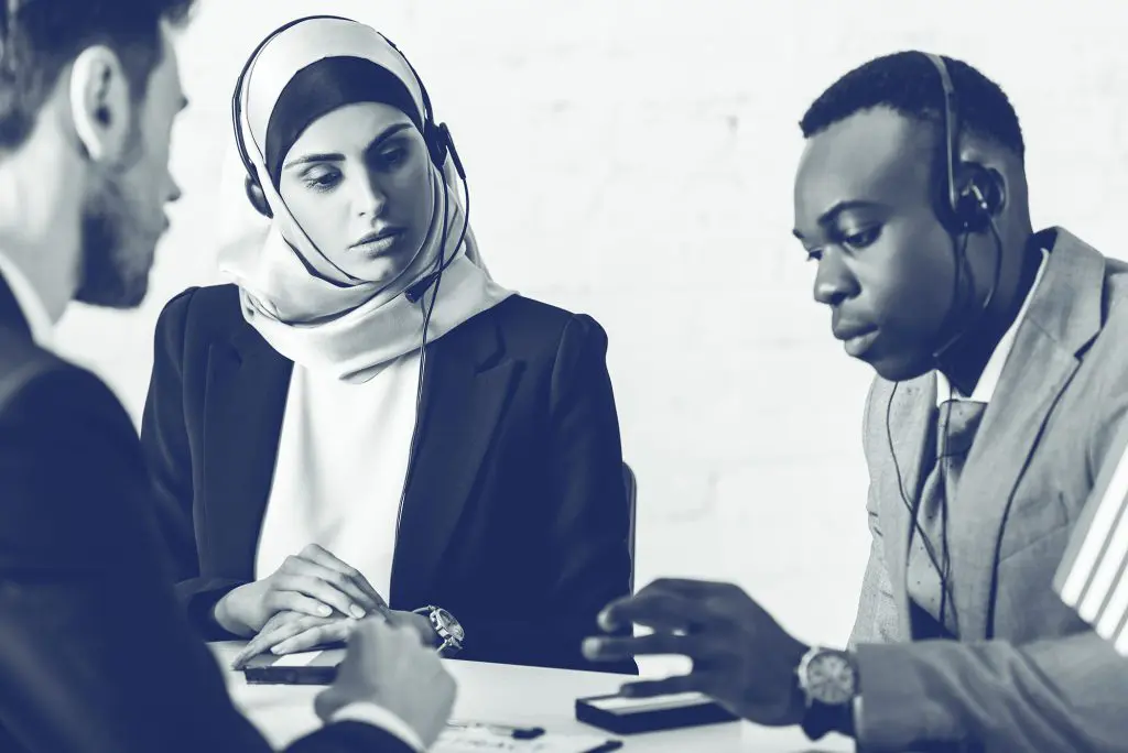 Three customer service agents in headsets sitting at a table, engaged in a serious discussion.