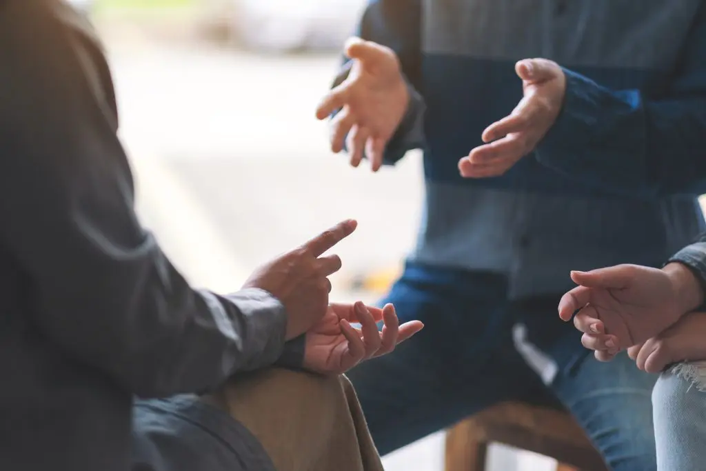 Three people sit together having a discussion, gesturing with their hands as they talk.