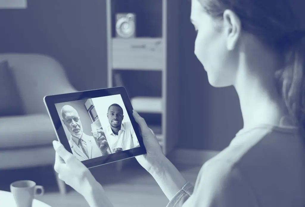 Woman holds tablet, video calling two men; one elderly in a suit, one younger in a white shirt.